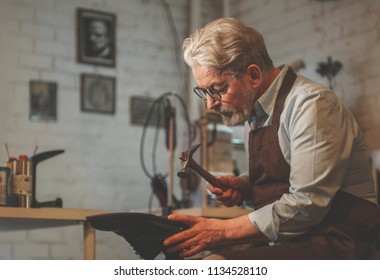 An elderly shoemaker at work in the workshop - Powered by Shutterstock