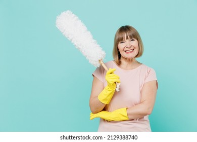 Elderly smiling cool housewife woman 50s in pink t-shirt gloves doing housework hold white duster brush isolated on plain pastel light blue background studio. Housekeeping cleaning tidying up concept