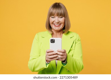 Elderly smiling fun woman 50s years old wearing green jacket white t-shirt hold in hand use mobile cell phone send message isolated on plain yellow background studio portrait. People lifestyle concept - Powered by Shutterstock