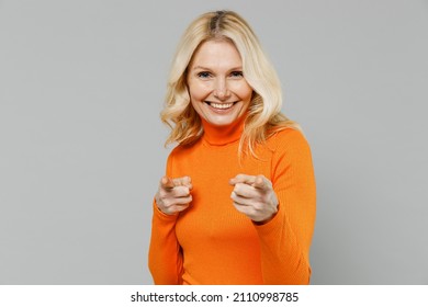 Elderly Smiling Happy Blonde Caucasian Woman 50s In Orange Turtleneck Point Index Finger Camera On You Say Do It Motivate Isolated On Plain Grey Background Studio Portrait. People Lifestyle Concept