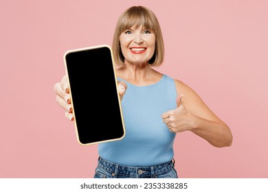 Elderly smiling happy blonde woman 50s years old wear blue undershirt casual clothes hold in hand use mobile cell phone with blank screen workspace area show thumb up isolated on plain pink background - Powered by Shutterstock