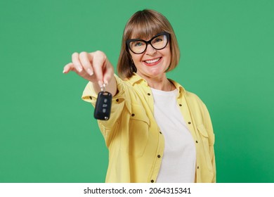 Elderly Smiling Happy Cheerful Caucasian Woman 50s In Glasses Yellow Shirt Hold In Hand Giving Car Keys Fob Keyless System Isolated On Plain Green Background Studio Portrait People Lifestyle Concept.