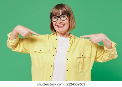 Elderly Smiling Happy Confident Cool Fun Caucasian Woman 50s In Glasses Yellow Shirt Point Index Finger On Herself Isolated On Plain Green Color Background Studio Portrait People Lifestyle Concept.