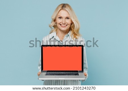 Elderly smiling happy fun caucasian woman 50s wearing striped shirt hold use work on laptop pc computer with blank screen workspace area isolated on plain pastel light blue color background studio.