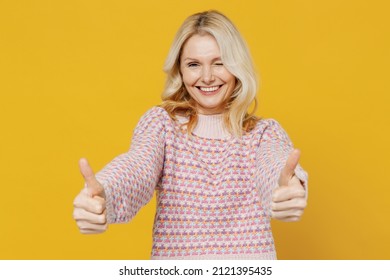 Elderly Smiling Satisfied Cheerful Blonde Caucasian Woman 50s In Pink Sweater Showing Thumb Up Like Gesture Blink Isolated On Plain Yellow Color Background Studio Portrait. People Lifestyle Concept