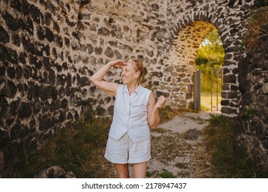 Elderly Smiling Senior Traveling Mature Woman Tourist Walking Posing Outdoors In Ancient Europe Fortress. Retired People Summer Holiday Vacation, Active Lifestyle Concept