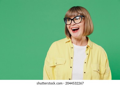 Elderly Smiling Surprised Amazed Happy Caucasian Woman 50s Wear Glasses Yellow Shirt Look Aside On Workspace Copy Space Area Isolated On Plain Green Background Studio Portrait People Lifestyle Concept