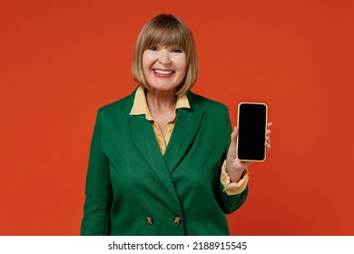 Elderly Smiling Woman 50s In Green Classic Suit Hold In Hand Using Mobile Cell Phone With Blank Screen Workspace Area Isolated On Plain Orange Color Background Studio People Business Lifestyle Concept