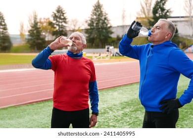 Elderly sportsmen in colorful attire drink water while taking a break from running on an athletic track, embodying active lifestyle - Powered by Shutterstock