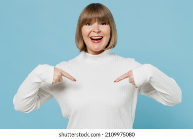 Elderly surprised amazed exultant jubilant fun woman 50s wearing white knitted sweater point index finger on herself isolated on plain blue color background studio portrait. People lifestyle concept
