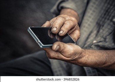 Elderly & Technology. Senior Old Man Using Phone Isolated Dark Black Background. Closeup Cropped Image Wrinkled Hands Holding Cellphone. Past & Future Symbol Concept Focus On Upper Hand And Reflection