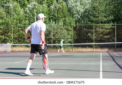 An Elderly Tennis Player Walks Along The Net On An Outdoor Court