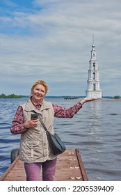 An elderly tourist poses against the background of the bell tower and pretends to hold the tower in the palm of her hand. Travel photos.