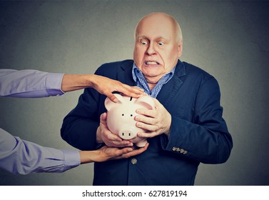 Elderly upset scared business man holding piggy bank trying to protect his savings from being stolen isolated gray background