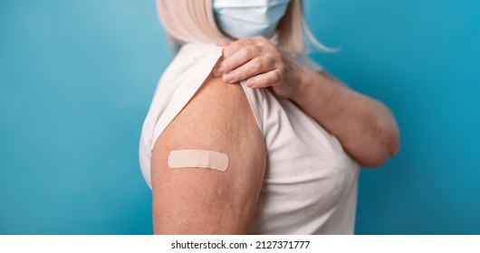 Elderly Vaccination. Healthy Mature Older Senior 50s Woman Showing Arm With Plaster After Vaccine, Wearing Face Mask Over Blue Background.