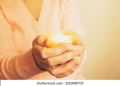 Elderly Veteran Woman Holding Burning Candle In Aged Wrinkled Hands For Memorial Day. Senior Old Lady Holocaust Surviver On Remembrance Weekend Sitting In Darkness & Candlelight. Close Up, Copy Space.