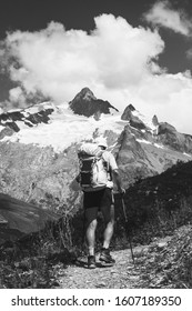 Elderly Wellness Concept. Senior Man Hiking French Alps In Summer With Solar Backpack.  Aiguille Des Glaciers, Mont Blanc Mountains. View From Chapieux Valley, Savoie, France. Black White Photo