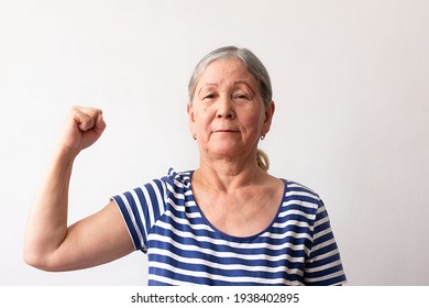 Elderly Woman, 60s Gray-haired Lady In Striped White And Blue Dress, Strong Man Showing Arm Muscles, Confident And Proud Of His Power On White Background.