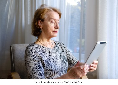 Elderly Woman 65-70 Years Old Having Conversation With Someone Via Tablet Pc At Home. Senior Woman Watching Video Using Tablet Computer. Concept Of Lifestyle, Technology.