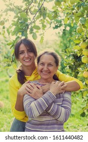   Elderly Woman With   Adult Daughter In   Apple Orchard.