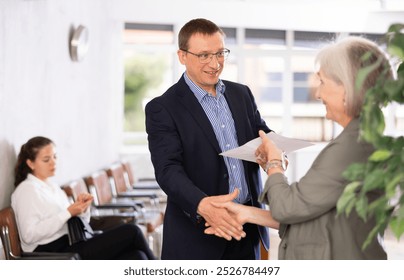 Elderly woman and adult man making agreement shaking hands in reception - Powered by Shutterstock