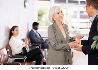 Elderly woman and adult man shaking hands after making deal in reception.. - Powered by Shutterstock