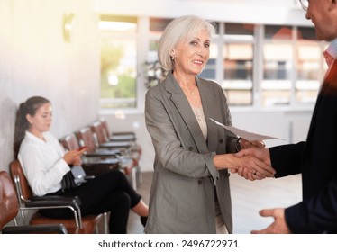 Elderly woman and adult man shaking hands after making deal in reception.. - Powered by Shutterstock