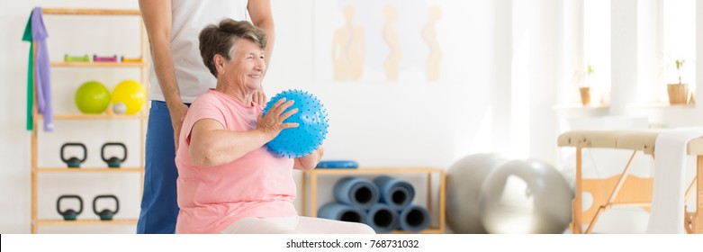 Elderly Woman After Injury Doing Exercise With A Ball In Rehabilitation Center With Personal Physiotherapist