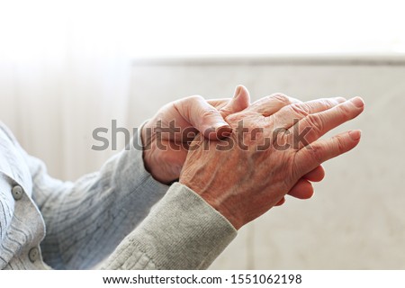 Elderly woman applying moisturizing lotion cream on hand palm, easing aches. Senior old lady experiencing severe arthritis rheumatics pains, massaging, warming up arm. Close up, copy space, background