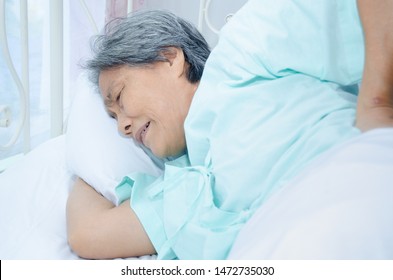 Elderly Woman Asians Have Back Pain.An Old Woman Wearing A Green Shirt Sleeping On The Bed In The Room. Elderly People Are Not Comfortable.Lady Have White Hair On Their Heads.