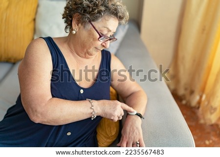 Elderly woman asking for help by pressing the telecare button on her wristband. Emergency Button Concept. Medical alert concept.