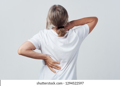 Elderly woman with back pain holding her lower back and neck on gray background