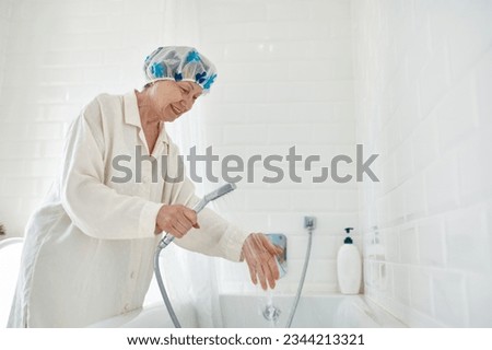 Elderly woman in bathrobe filling bathtub with water