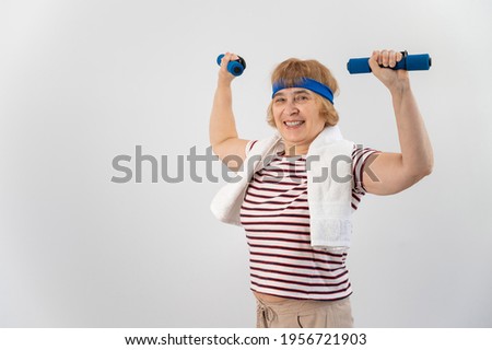 An elderly woman with a blue bandage on her head trains with dumbbells on a white background