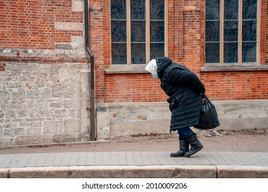 Elderly woman in a blue mask, hunched over, walks down the street