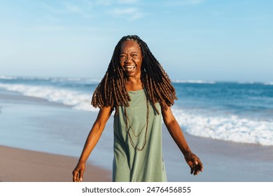 Elderly woman with braided hair enjoying a casual walk on the beach at sunset. She is smiling and exuding happiness. - Powered by Shutterstock