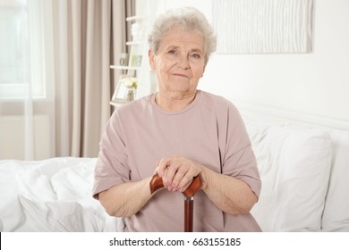 Elderly woman with cane sitting on bed at home - Powered by Shutterstock