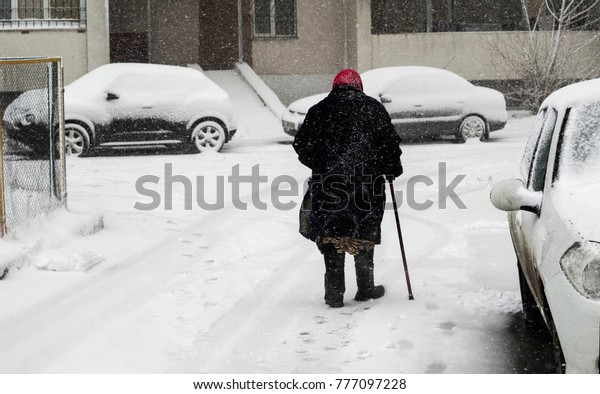 elderly woman with a cane walking\
by Cars Covered With Fresh White Snow After A Heavy Blizzard\
