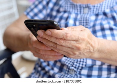 Elderly woman in checkered dress sitting with smartphone in chair, mobile phone in wrinkled female hands closeup. Concept of online communication in retirement - Powered by Shutterstock