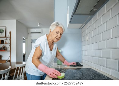 Elderly woman cleaning kitchen stove at home - Powered by Shutterstock