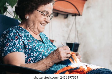 Elderly woman crocheting a blanket. She is sitting in a chair in the patio of her house. She is concentrating on her task. - Powered by Shutterstock