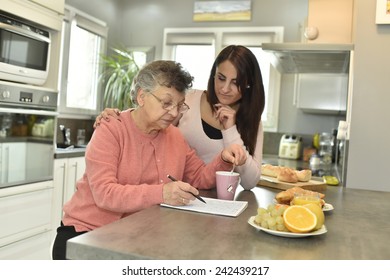 Elderly Woman Doing Crossword While Homecare Helps At Home