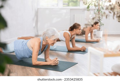 Elderly woman doing pilates exercises in group in fitness studio - Powered by Shutterstock