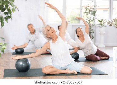 Elderly woman doing pilates exercises with soft ball in fitness studio with group - Powered by Shutterstock