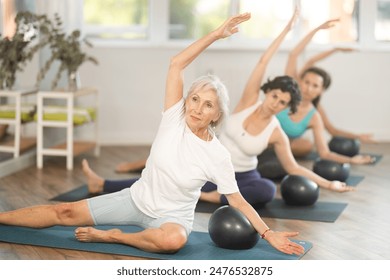 Elderly woman doing pilates with soft ball in group in fitness studio - Powered by Shutterstock