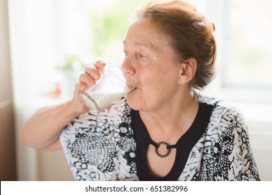 Elderly Woman Drinking Milk From Glass In Her Kitchen