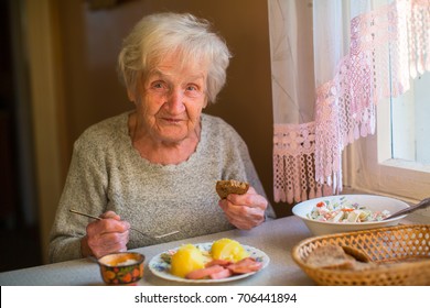 An elderly woman eat sitting at dinner table at home.