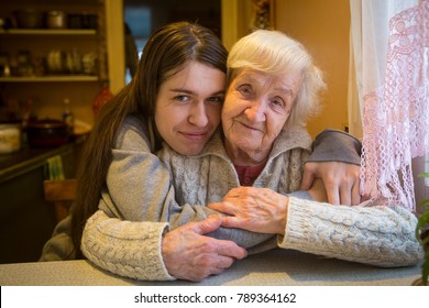 An elderly woman in an embrace with an adult granddaughter posing for the camera in a village house.