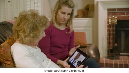 An elderly woman engages in a video consult with her doctor via wireless tablet as her daughter listens.