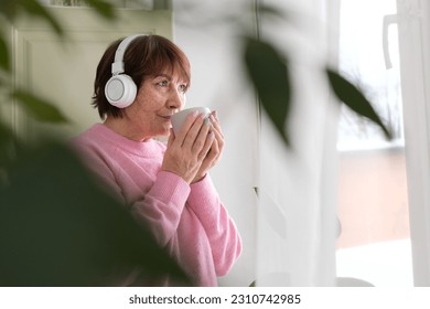 Elderly woman enjoying coffee music by the window. embracing modern life - Shutterstock ID 2310742985